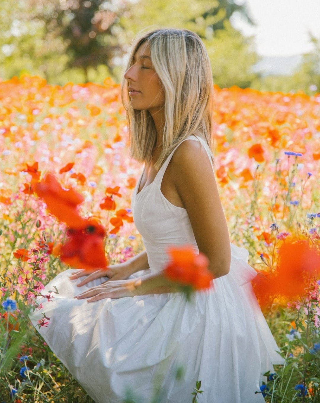 a woman in a white dress sitting in a field of flowers